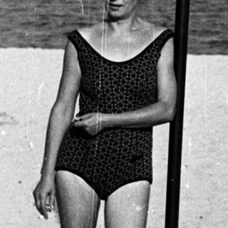 Woman stands on a beach with a pole in black and white.