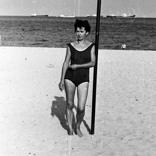 Woman stands on a beach with a pole in black and white.