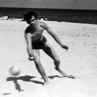 Boy kicking a ball on a sandy beach.