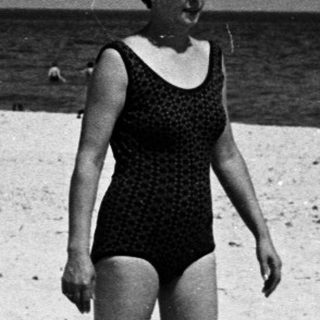 Woman in a bathing suit stands on a sandy beach.