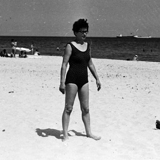 Woman in a bathing suit stands on a sandy beach.