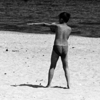 Children playing on a beach with ships in the distance.