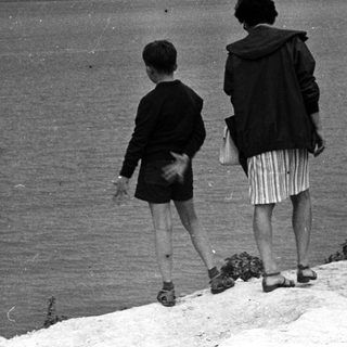 Three figures view a seascape from a coastal hillside.