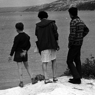 Three figures view a seascape from a coastal hillside.