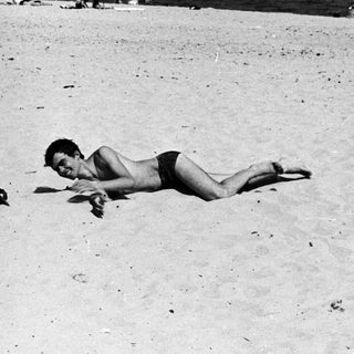 Man lies prone on a beach with ocean backdrop.