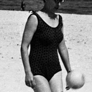 Woman walks on a beach, holding a ball.