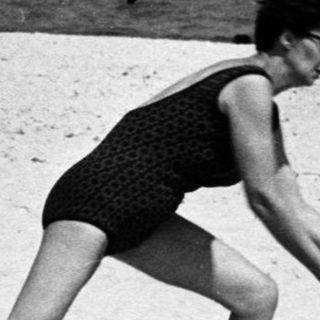 Woman throws ball on a crowded beach.