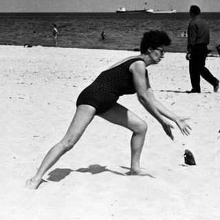 Woman throws ball on a crowded beach.