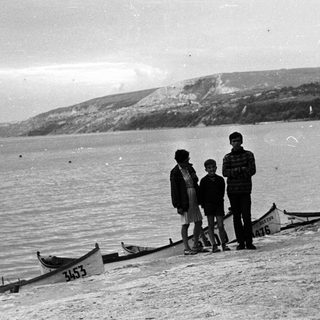 Black and white photo of people on a beach with boats.