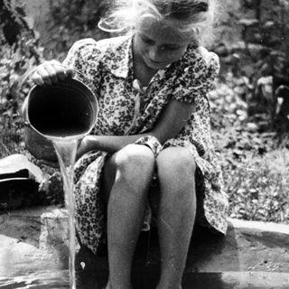 Girl pours water into a puddle in a garden.