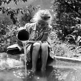Girl pours water into a puddle in a garden.