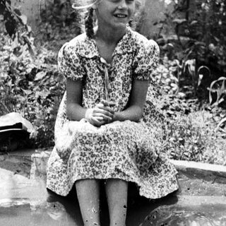 Girl sitting in water, smiling, surrounded by foliage.