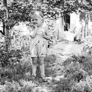Black and white photo of a toddler standing outdoors.