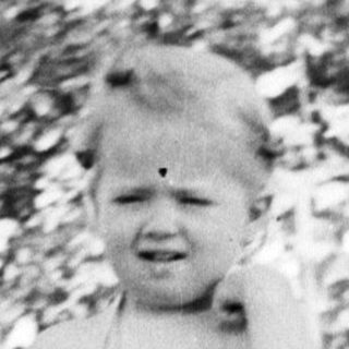 Black and white photo of a child standing outdoors.
