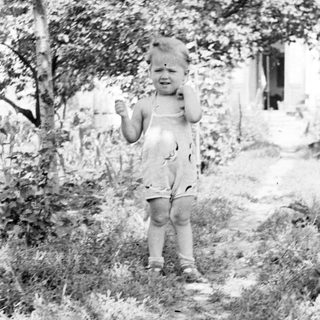 Black and white photo of a child standing outdoors.