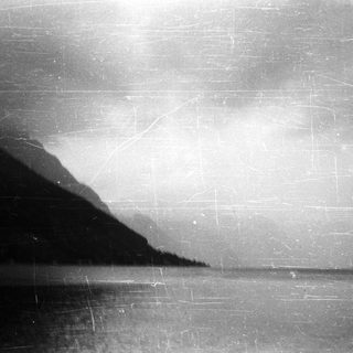 Dark, hazy landscape with mountains reflected in water.