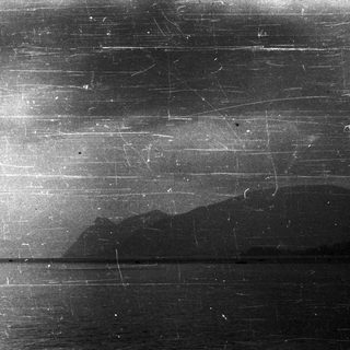 A dark, damaged photo depicting water and distant mountains.