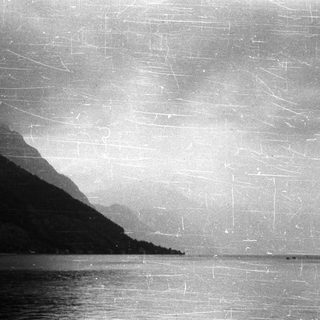 Monochrome landscape of mountains, water, and a cloudy sky.