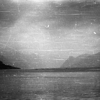 Monochromatic landscape of water and distant, hazy mountains.
