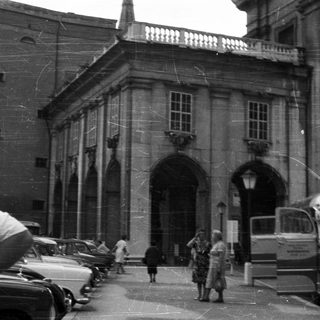 Black and white photo of a building, people, and vehicles.
