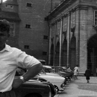 Black and white photo of a building, people, and vehicles.