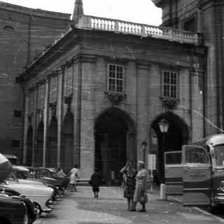 Black and white photo of a building, people, and vehicles.