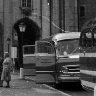 Black and white photo of a building, people, and vehicles.