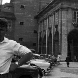 Black and white photo of a building, people, and vehicles.