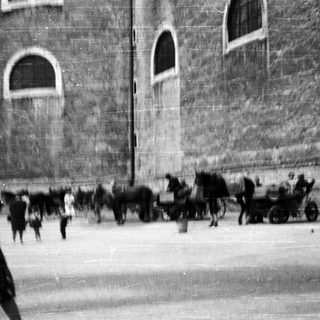 Here's a brief summary of the image: Horse-drawn cart and people near a stone building.