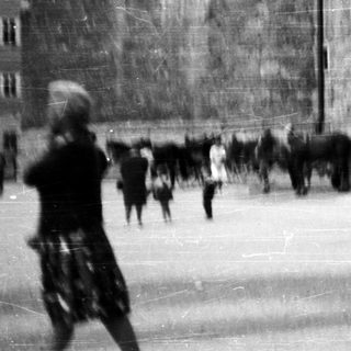Here's a brief summary of the image: Horse-drawn cart and people near a stone building.