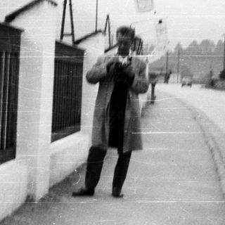 Man stands near a wall on a street.