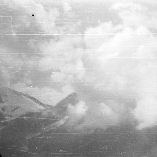Cloudy, grayscale landscape with mountains and visible scratches.
