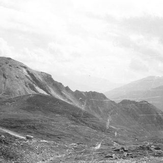 Monochrome landscape featuring mountains, a road, and cloudy sky.