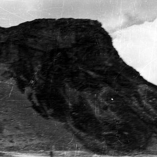 Black and white image of a cliff face and cloudy sky.