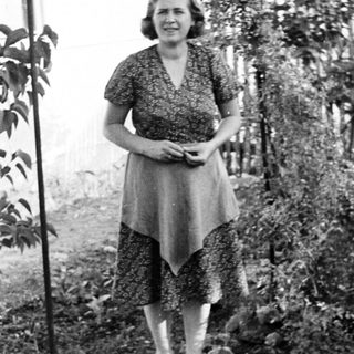 Woman stands in a garden wearing a patterned dress.