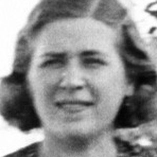 Woman stands in a garden wearing a patterned dress.