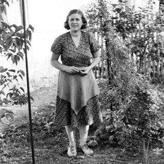 Woman stands in a garden wearing a patterned dress.