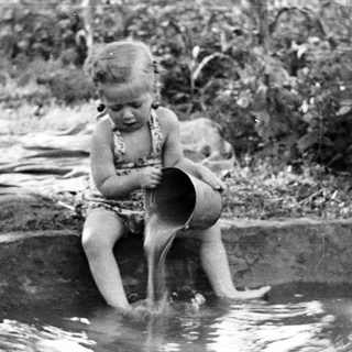 Here's a brief summary of the image: Child plays in a shallow pool outdoors.