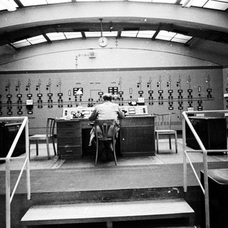 Man operating controls in a vintage control room.