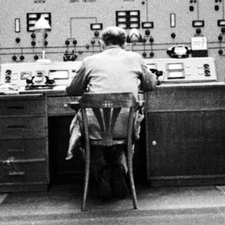 Man operating controls in a vintage control room.