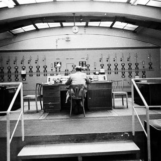 Man operating controls in a vintage control room.