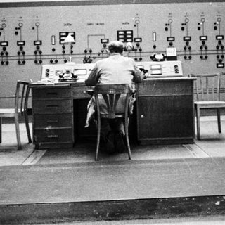 Man operating controls in a vintage control room.