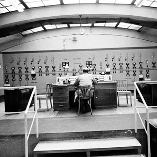 Man operates control panel in a vintage monitoring room.