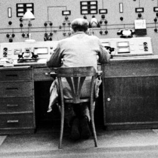 Man operates control panel in a vintage monitoring room.