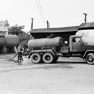 Tanker truck being filled near industrial buildings and storage tanks.