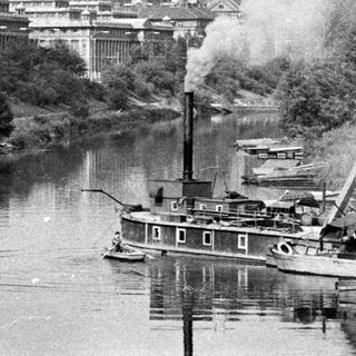Riverfront scene with a large building and steamboat.