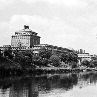 Large building overlooks river, reflected in water.