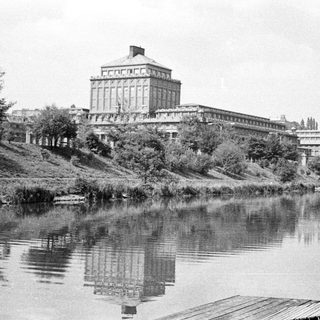 Large building reflected in a calm river landscape.