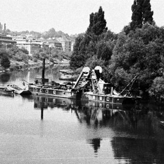River scene with dredging equipment and building in background.