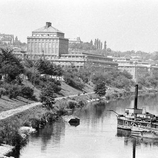 Riverfront view featuring a large building and docked boats.
